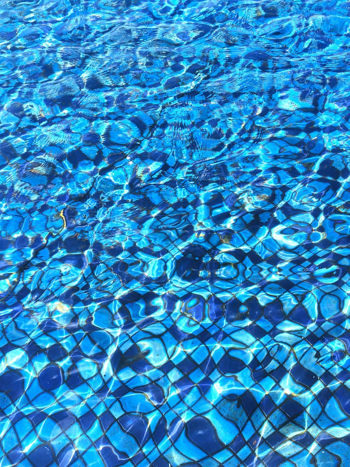 Menu A close-up view of rippling blue water in a pool, capturing light reflections and tile patterns.