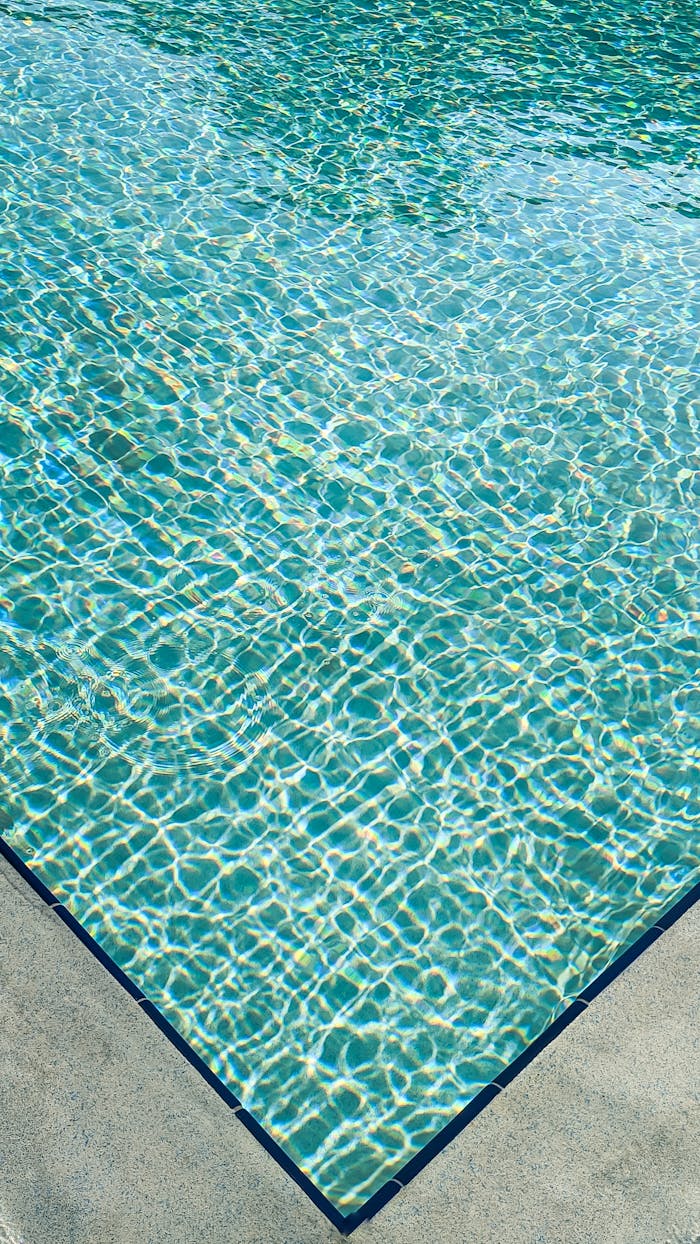 Home Vertical close-up of a turquoise swimming pool with rippling water and a concrete edge in bright sunlight.