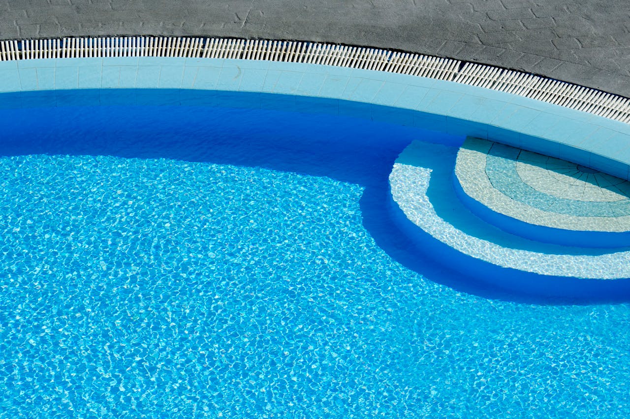 Menu Sun-drenched swimming pool captured from above, showcasing clear blue water and elegant curves.