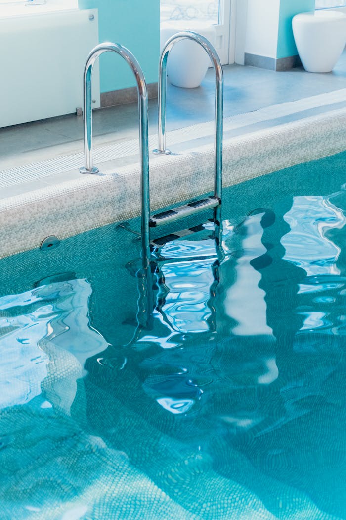Home A serene view of an indoor swimming pool with a metal ladder and clear water.